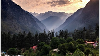 A mountainous landscape with a valley, dense forests, and a few buildings.