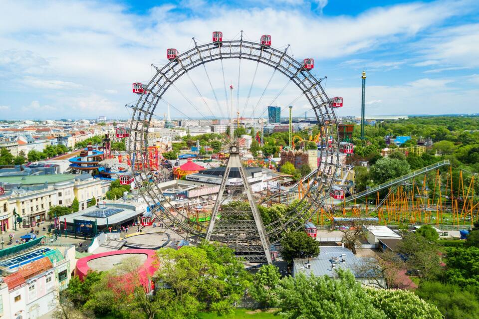 Uma grande roda gigante cercada por atrações de parque de diversões e edifícios.