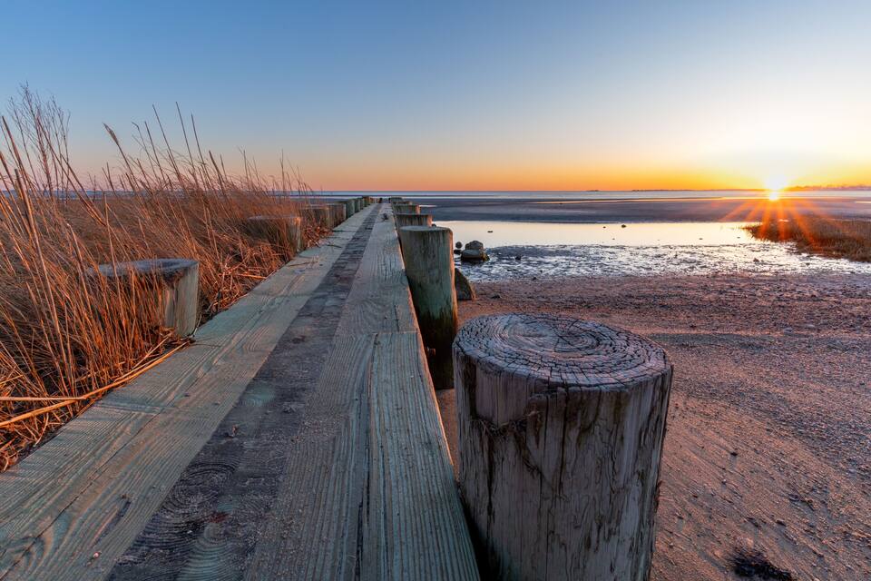 A wooden boardwalk leading to a beach at sunset.