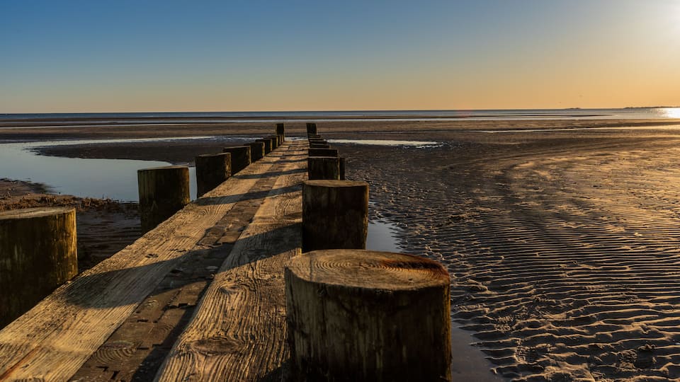A wooden boardwalk leading to a beach with calm waters and a clear sky.