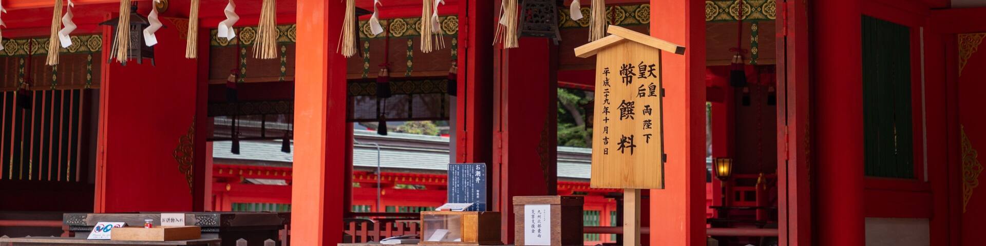 A traditional Japanese building with red pillars and a wooden sign with Japanese characters.