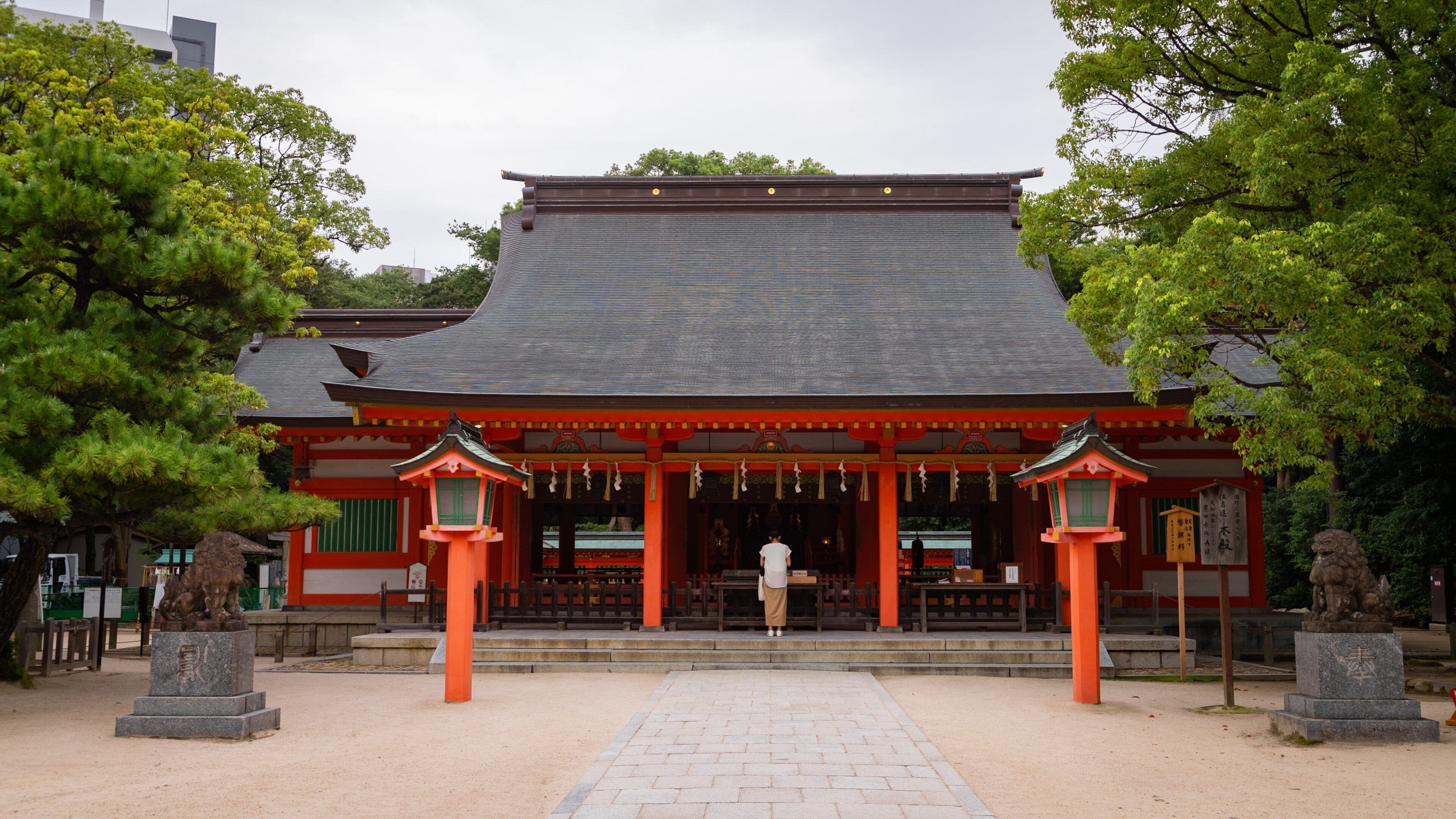 Un temple japonais traditionnel, avec un toit recouvert de tuiles, des piliers rouges et des lanternes en pierre.