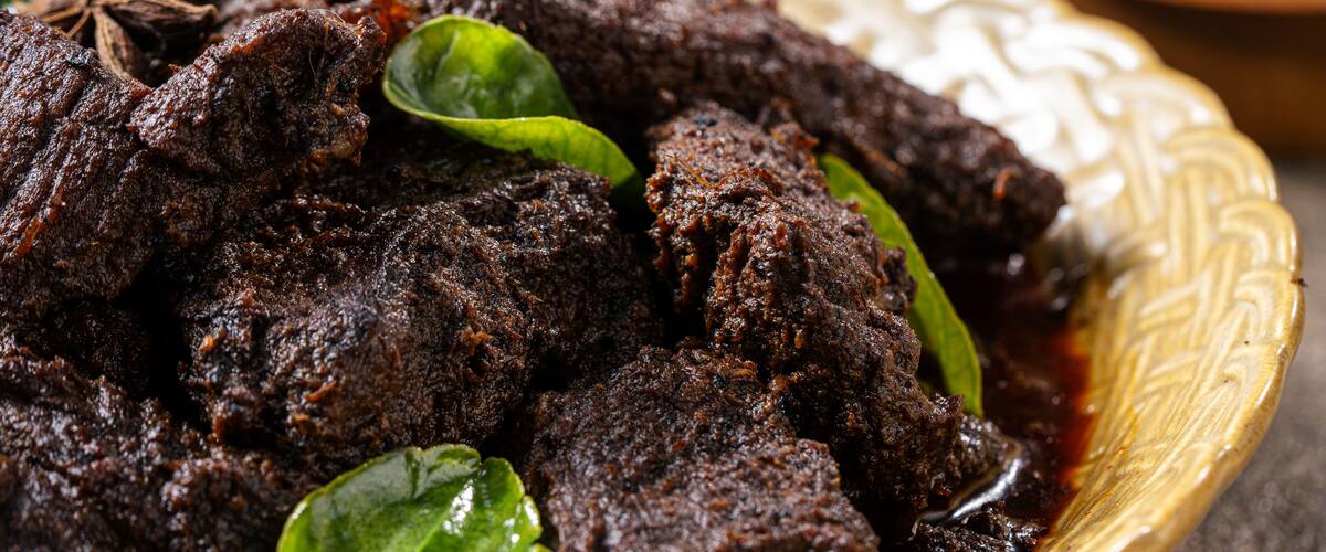 A bowl of dark, rich curry with green leaves and a star anise.