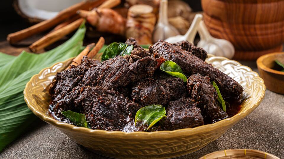 A bowl of dark meat with spices and leaves.