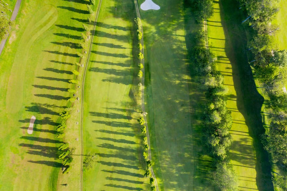 An aerial view of a green field with a road, trees, and a pond.