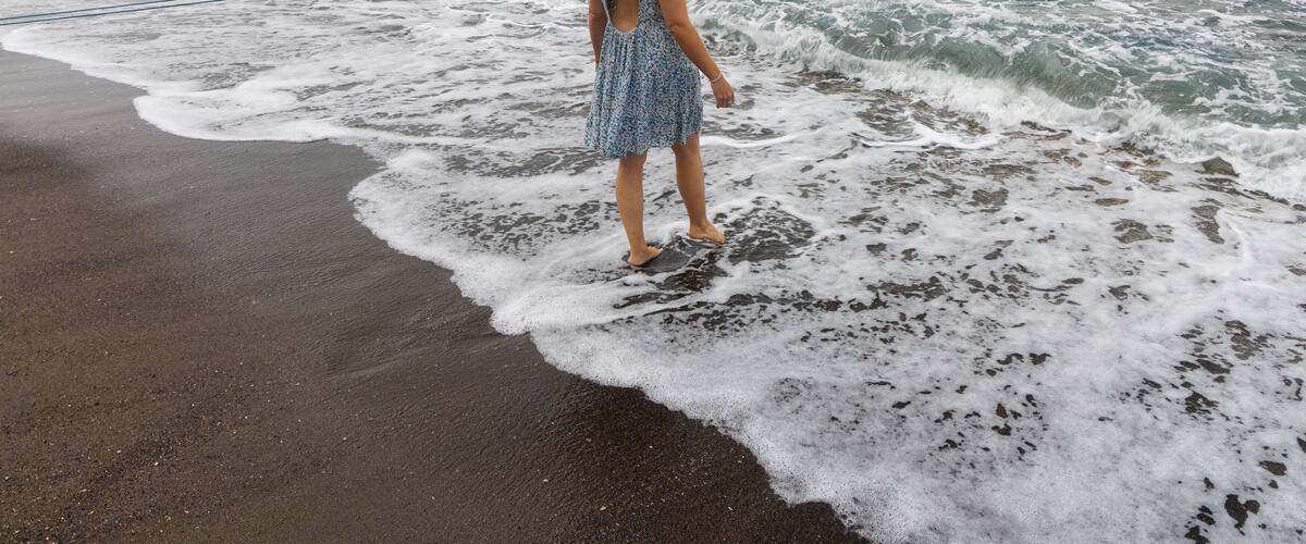 A woman standing on a beach with waves approaching.