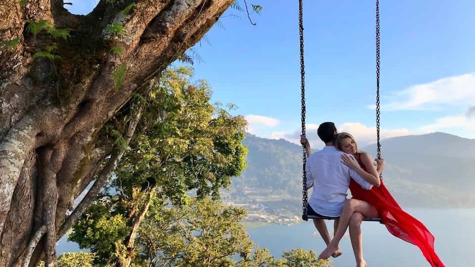 A couple on a swing overlooking a lake and mountains.