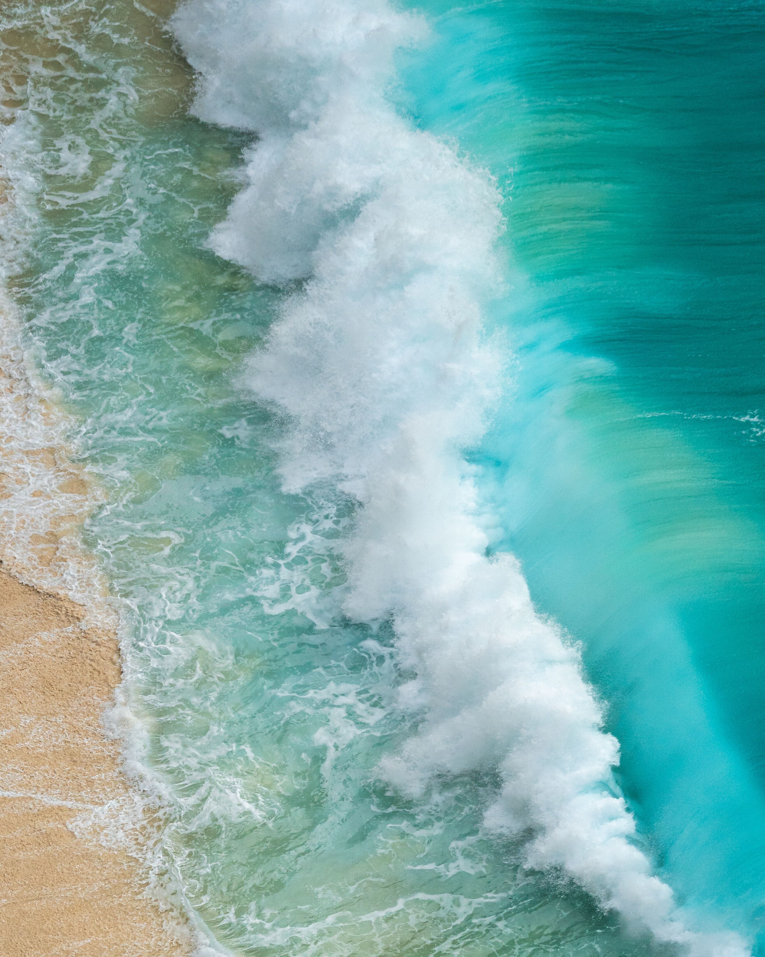 Aerial view of the turquoise ocean crashing against the sandy shore at Bunga Mekar, creating a mesmerizing contrast of colors and textures, Klungkung Regency, Bali, Indonesia.