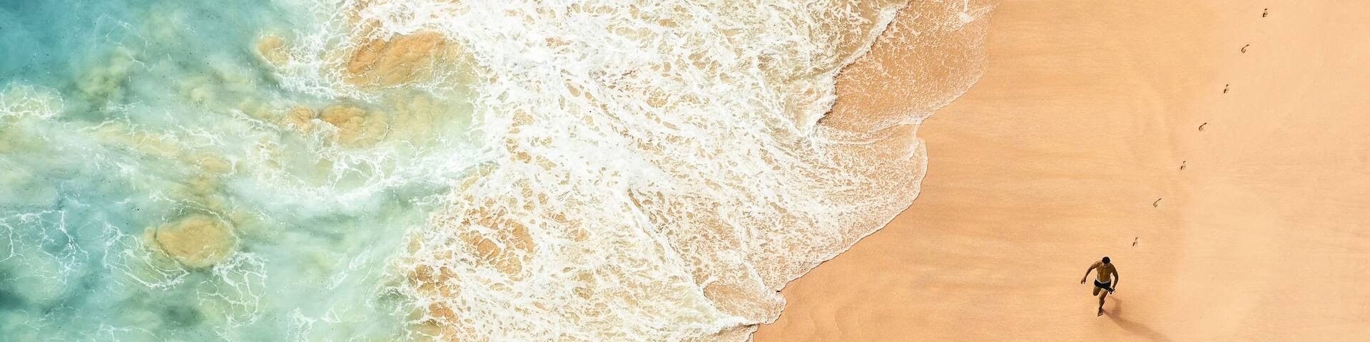 A sandy beach with waves and a single person walking.