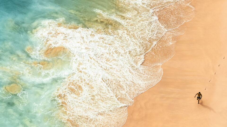 A sandy beach with waves and a single person walking.