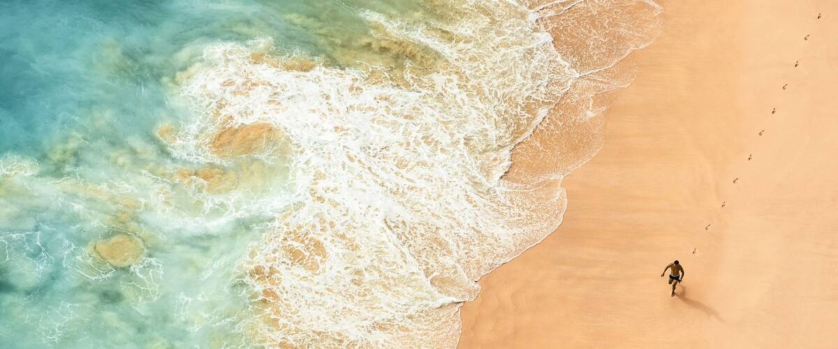A sandy beach with waves and a single person walking.