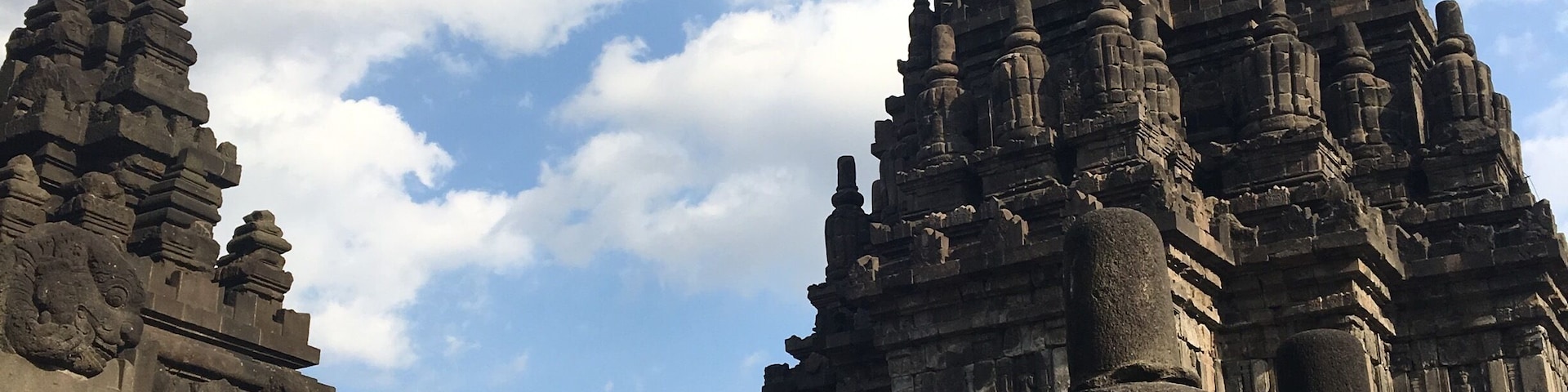 Estruturas de pedra antigas com esculturas detalhadas e um céu azul claro com nuvens.