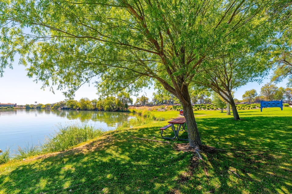 Un parque con un lago, mesas de picnic y un cartel azul.