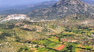 Paisagem montanhosa com campos em socalcos, um pico rochoso imponente e um pequeno povoado com construções.