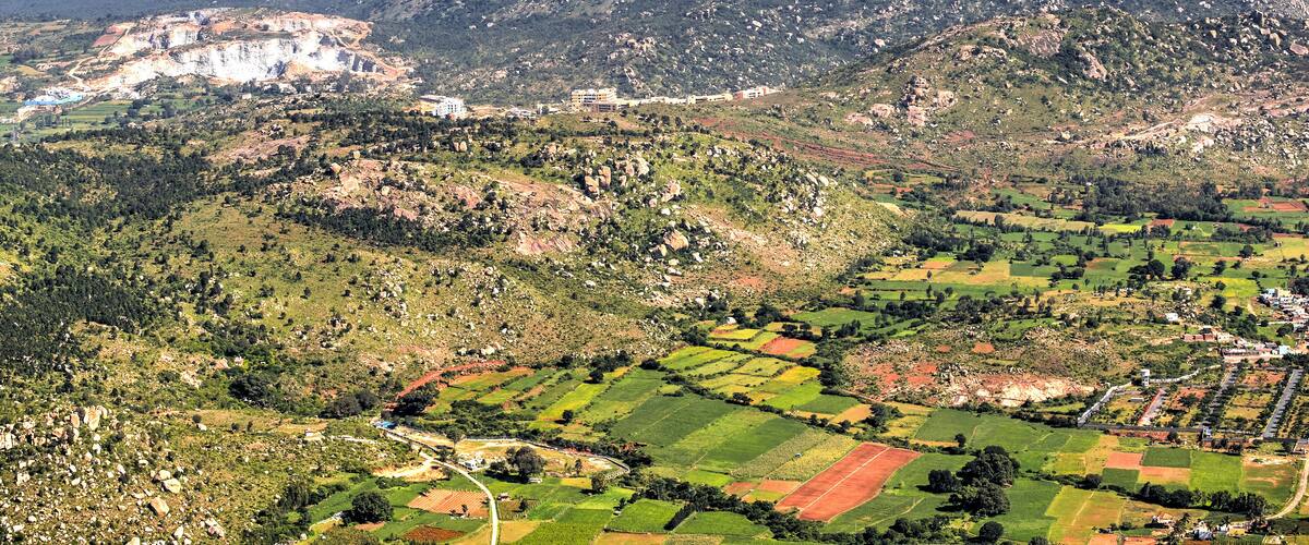 A mountainous landscape with terraced fields, a prominent rocky peak, and a small settlement with buildings.