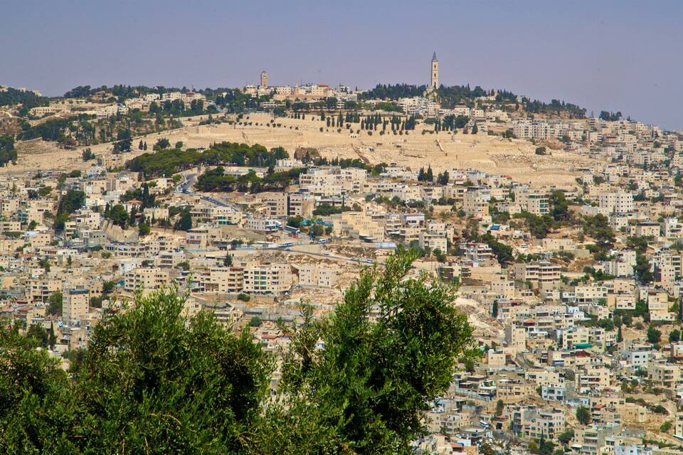A densely populated hillside city with numerous buildings, some with modern architecture, and a prominent tower on the hilltop.