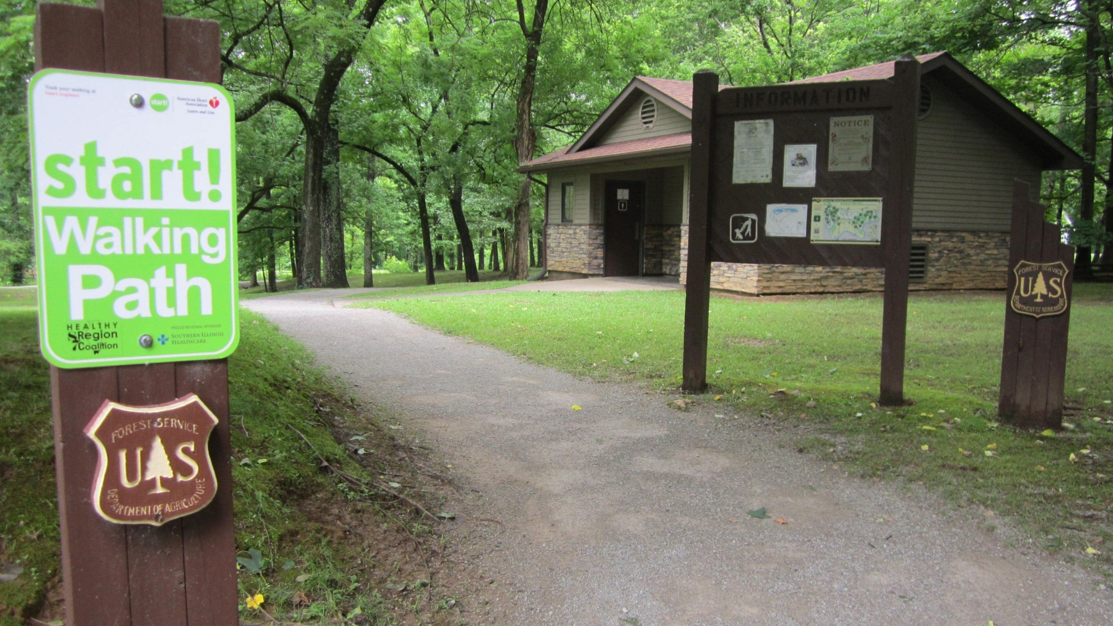 A walking path sign, a small cabin, and a forested area.