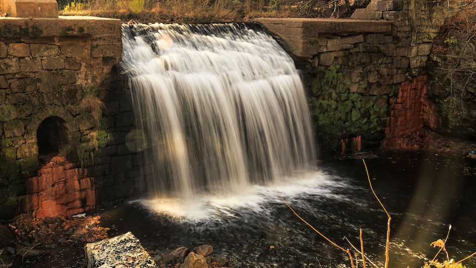 A waterfall cascading over stone walls into a river surrounded by trees.