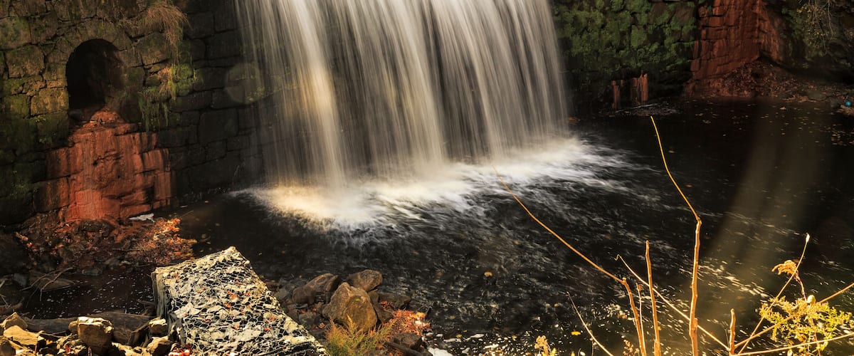 A waterfall cascading over stone walls into a river surrounded by trees.