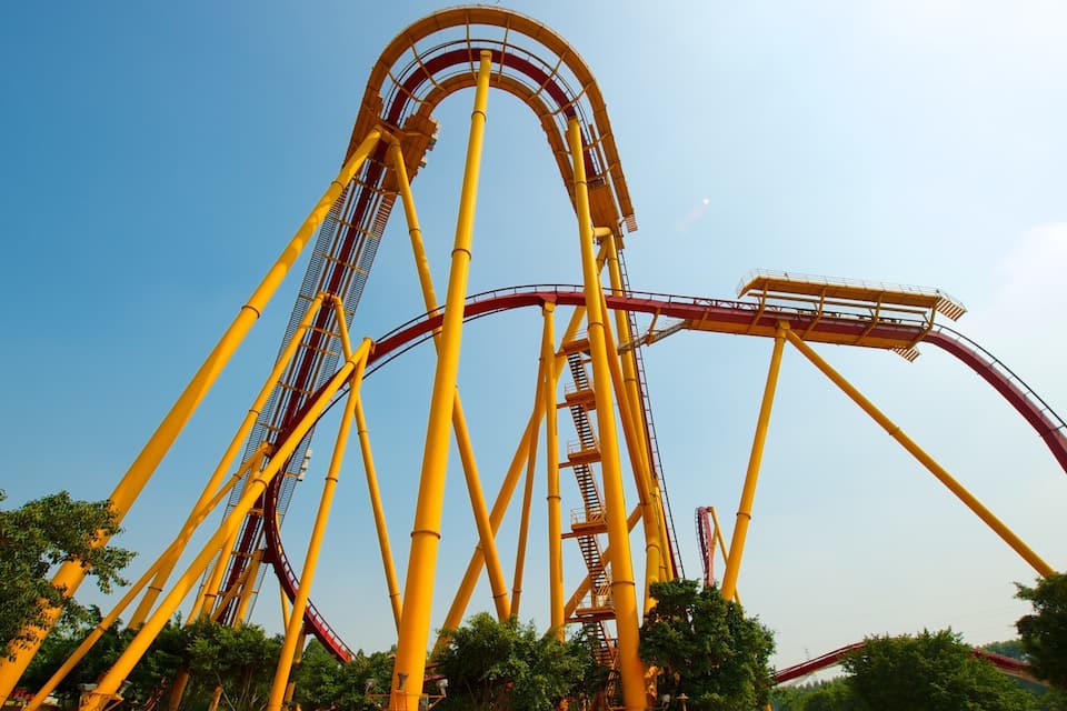 Una gran montaña rusa amarilla con rieles rojos contra un cielo azul despejado.