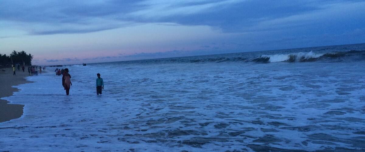A beach with waves and people walking.