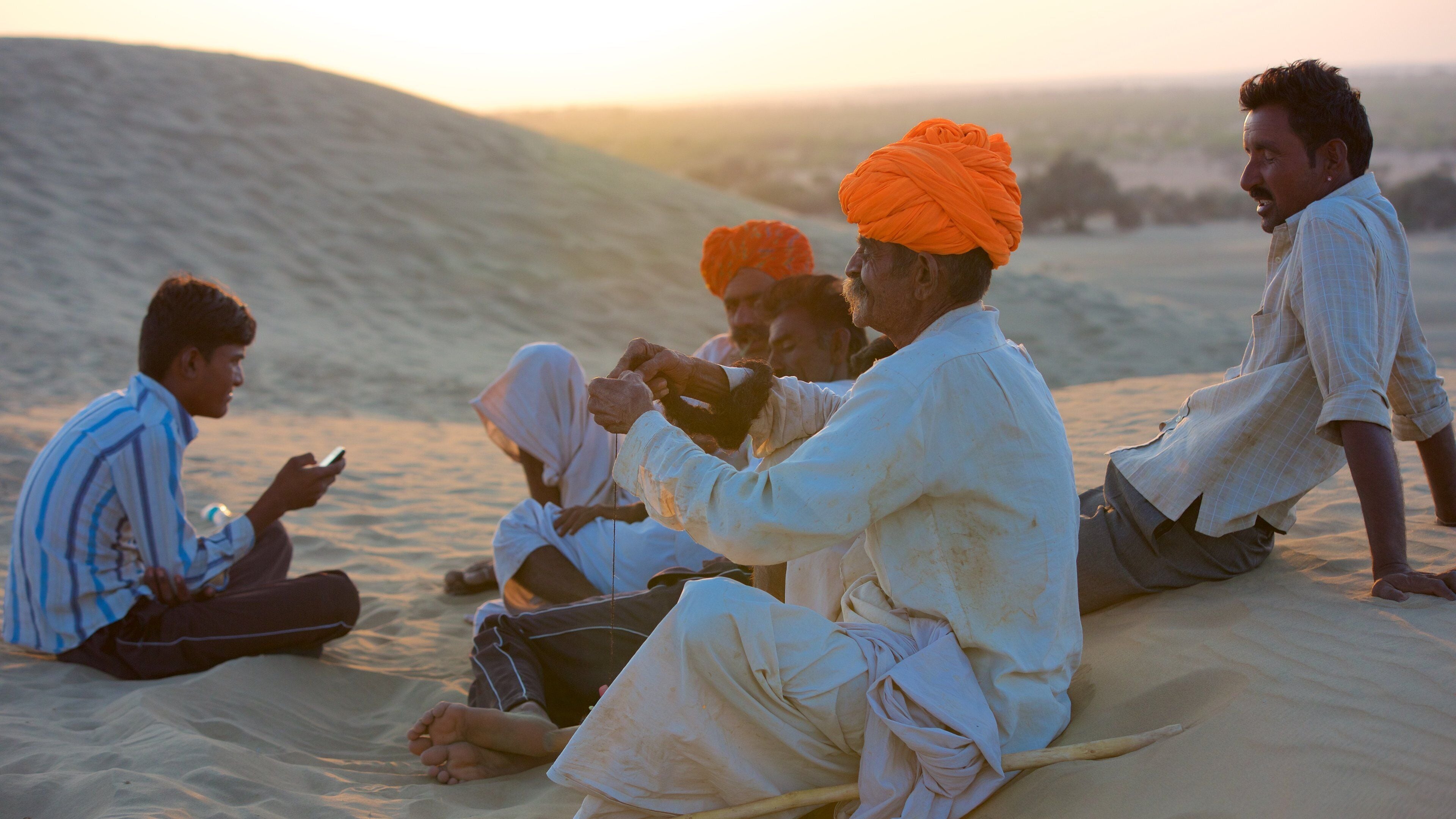 A group of people sitting on sand dunes during sunset.