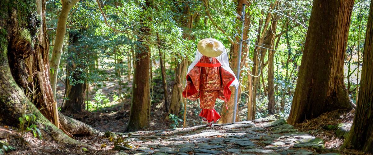 A forest path with a person in traditional attire walking away.