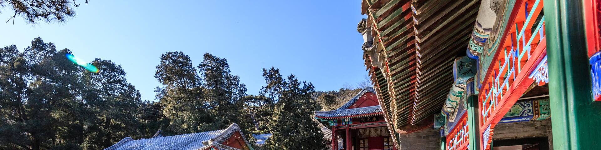 A traditional Chinese building with red and green colors, surrounded by snow-covered ground and trees.