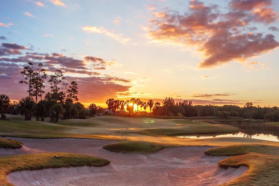 A golf course at sunset with sand bunkers and palm trees.
