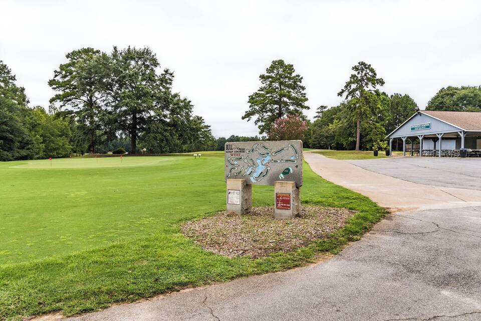 Un panneau indiquant le parcours de golf, un club-house et une pelouse bien entretenue, avec des arbres en arrière-plan.