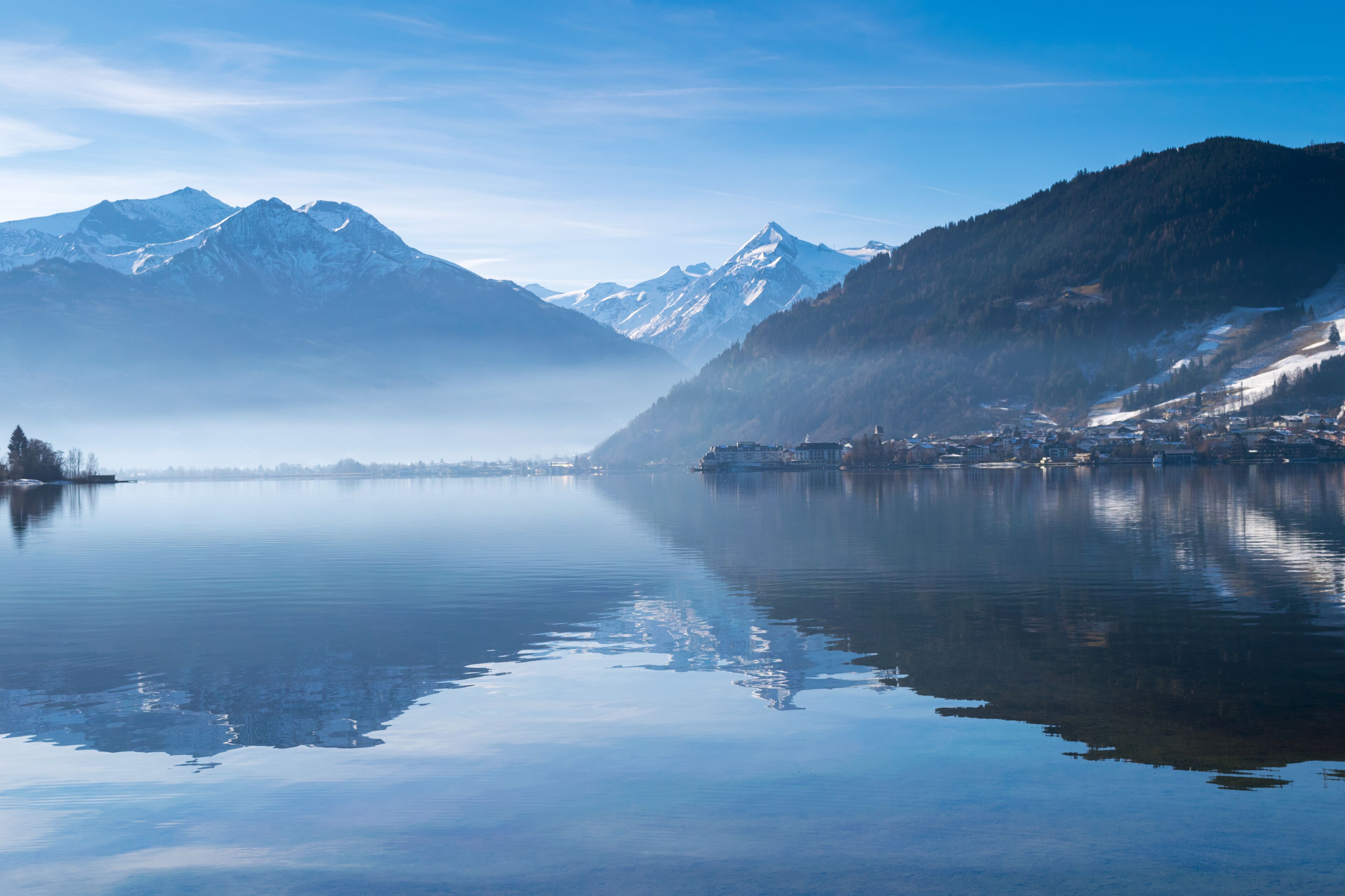 A calm lake with a mountain range in the background and a small town on the right.