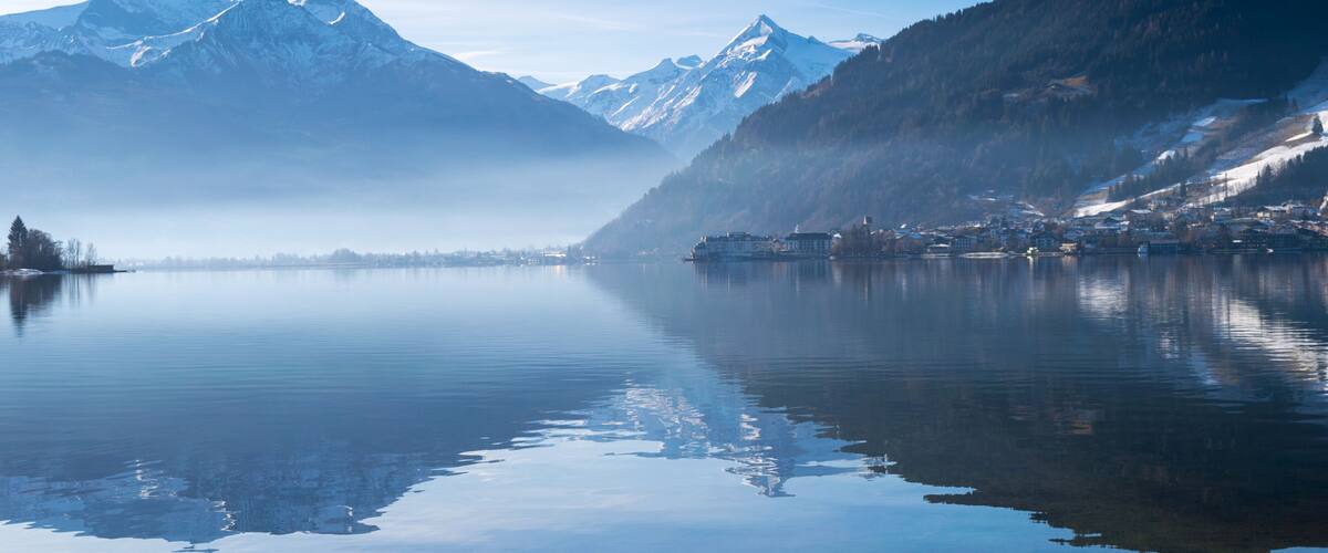 A calm lake with a mountain range in the background and a small town on the right.