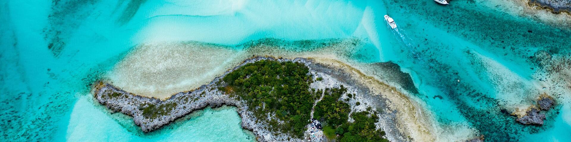 An aerial view of a tropical island with clear turquoise waters, a small dock, and a few buildings surrounded by lush greenery.
