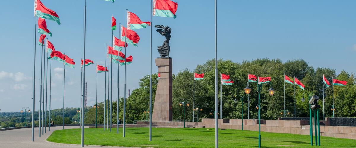 A monument with a statue, surrounded by flags on flagpoles, set against a clear sky.
