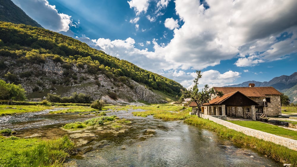 Une rivière traverse une vallée, et une maison en pierre se trouve sur la rive droite.