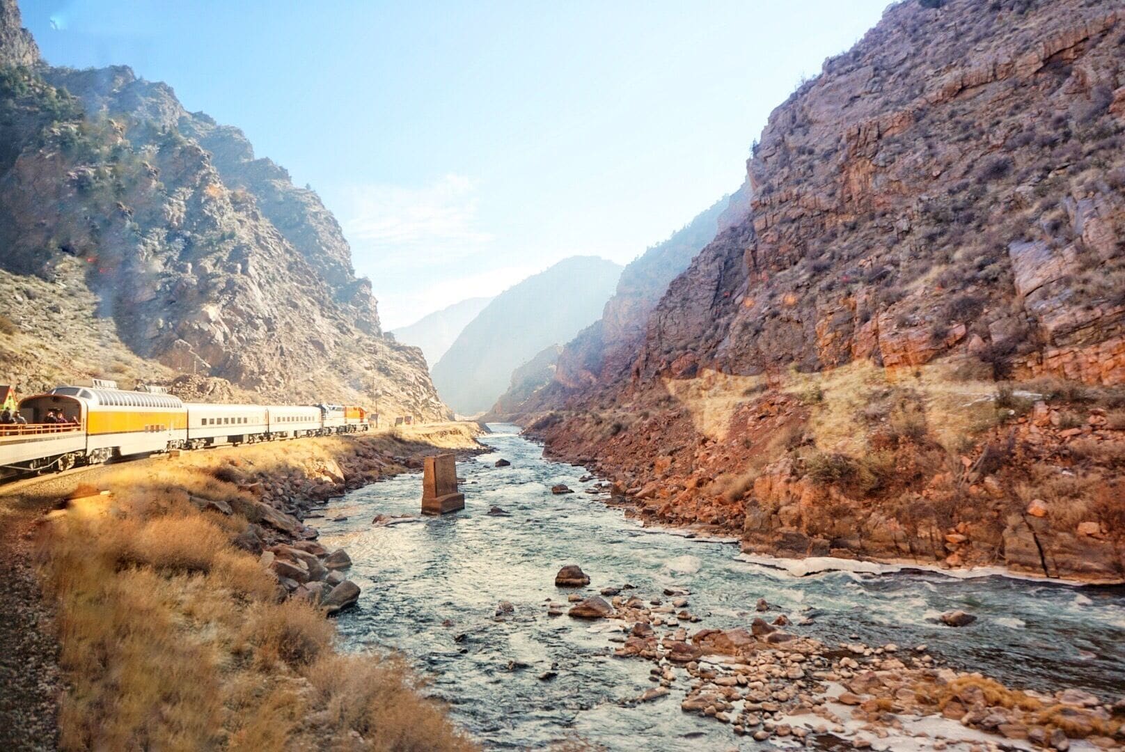 A train traveling through a canyon with a river running through it.