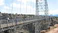 Un pont suspendu sur lequel des personnes se promènent, entouré d’un paysage rocheux et avec des montagnes en arrière-plan.