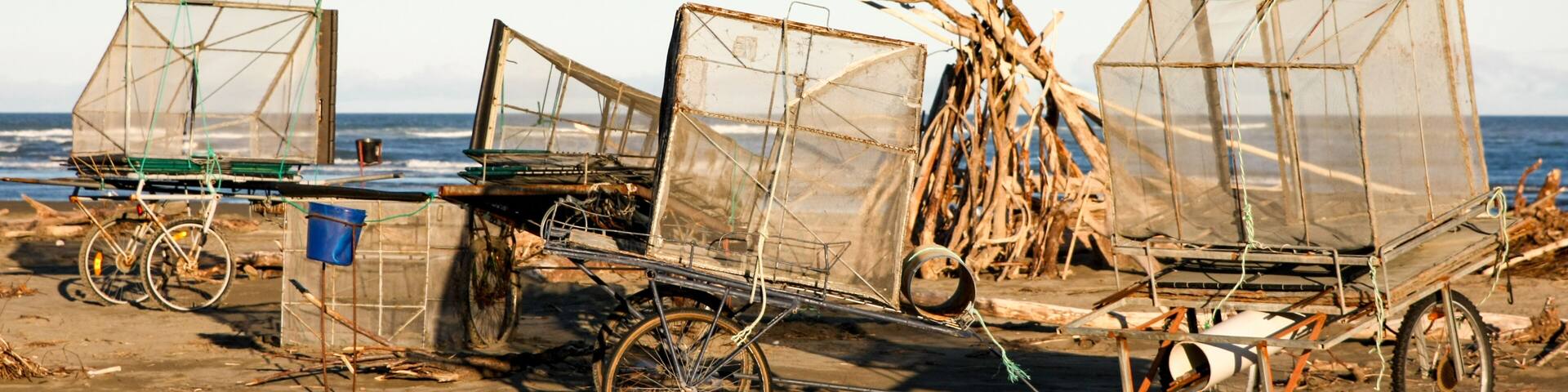A beach with three makeshift fishing boats with nets, a bicycle, and a blue bucket.