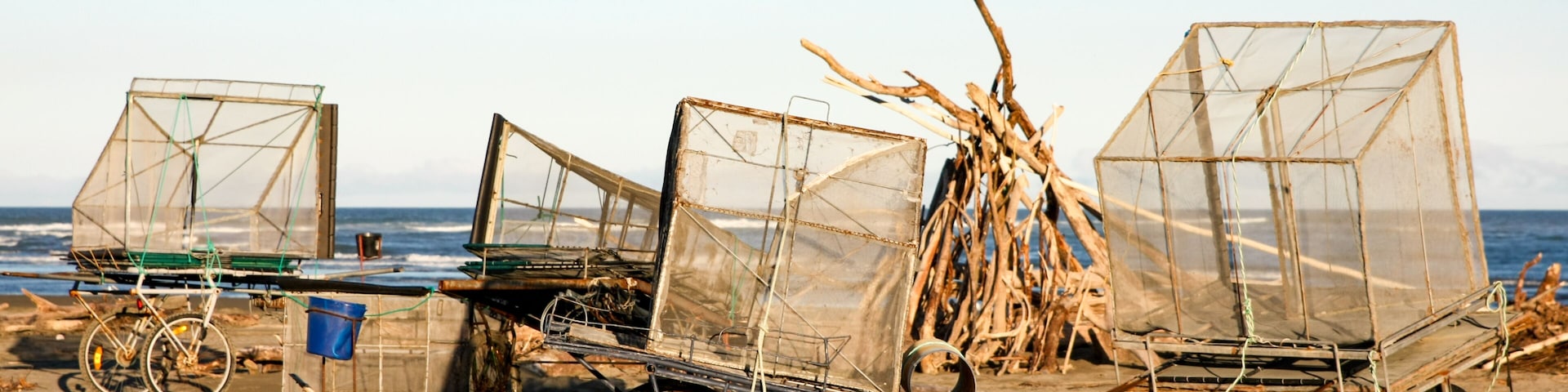 A beach with three makeshift fishing boats with nets, a bicycle, and a blue bucket.
