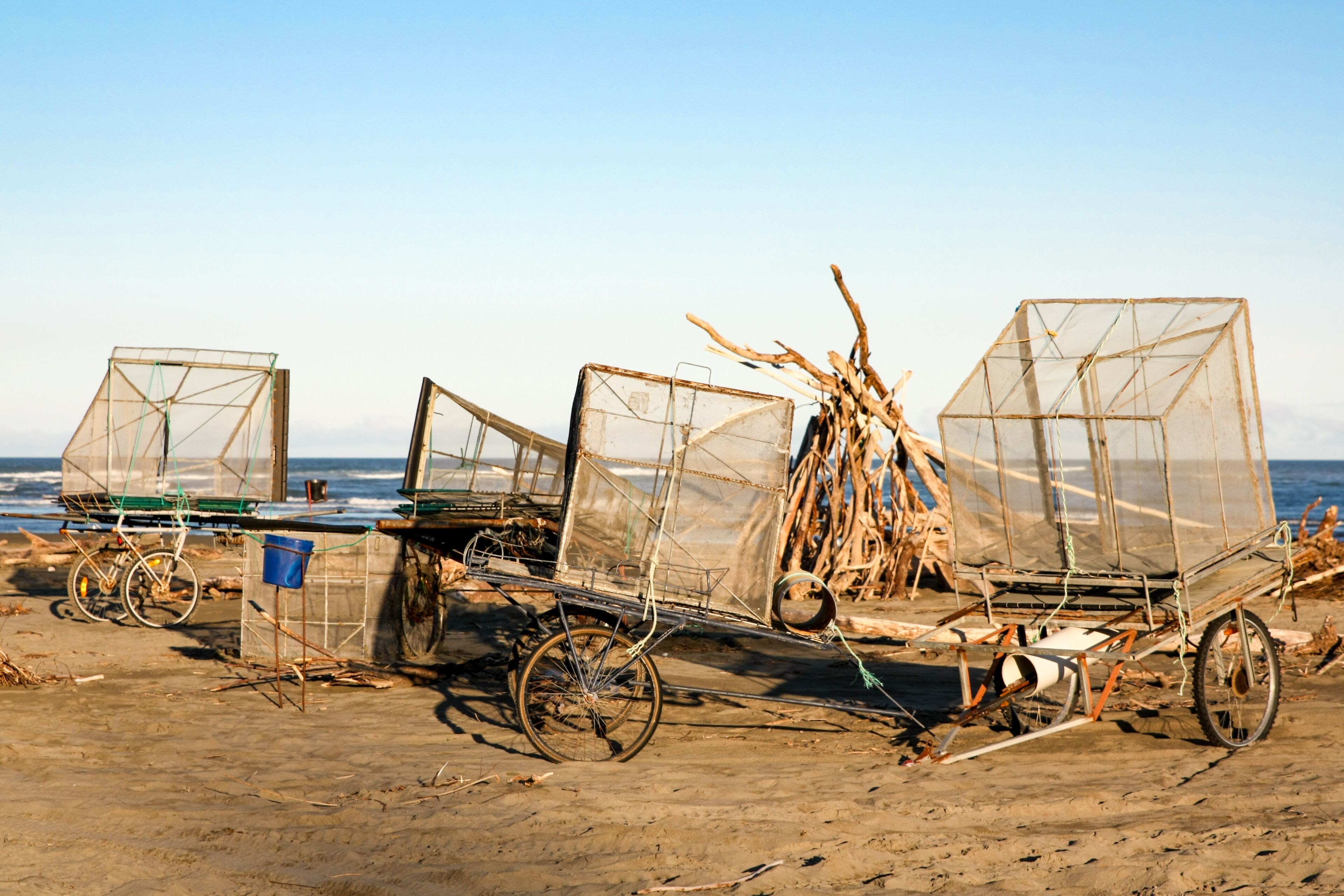 A beach with three makeshift fishing boats with nets, a bicycle, and a blue bucket.