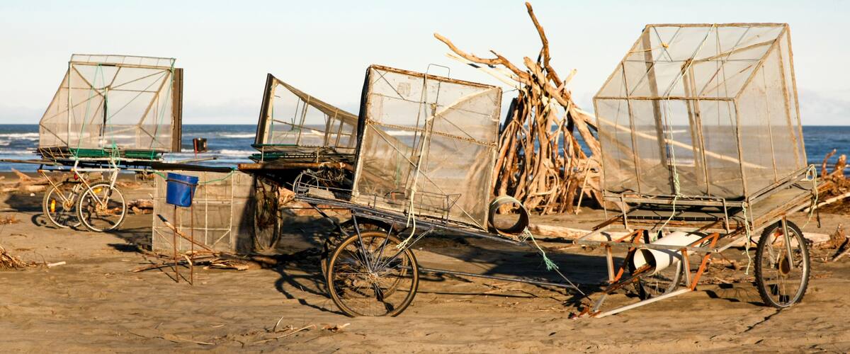 A beach with three makeshift fishing boats with nets, a bicycle, and a blue bucket.