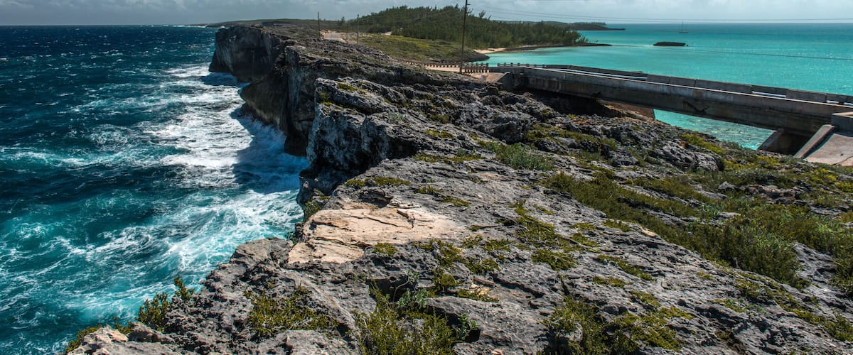 A rugged coastline with a bridge, ocean waves, and a distant island.