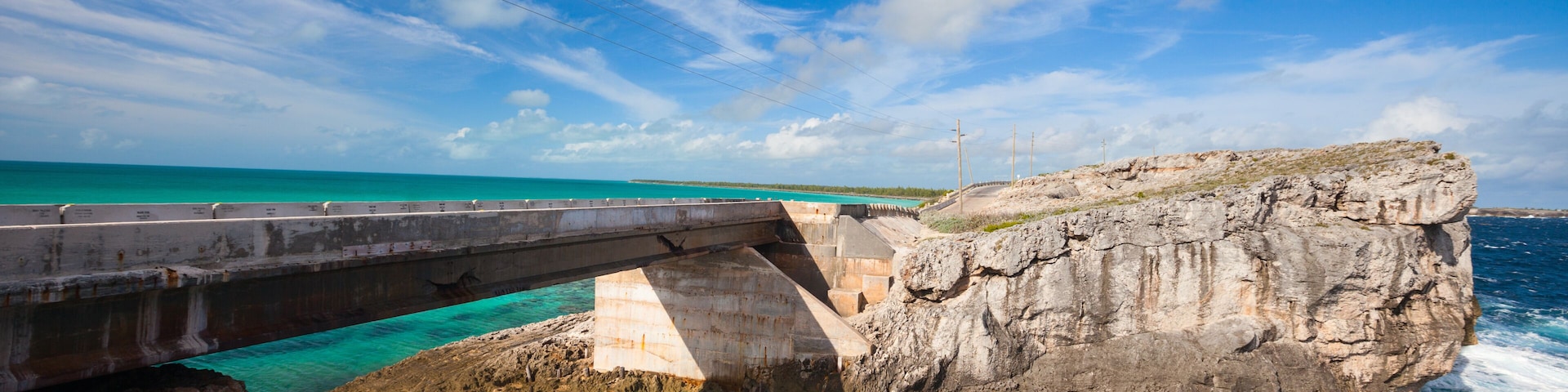 Un puente costero sobre aguas turquesas, acantilados rocosos y cielo despejado.