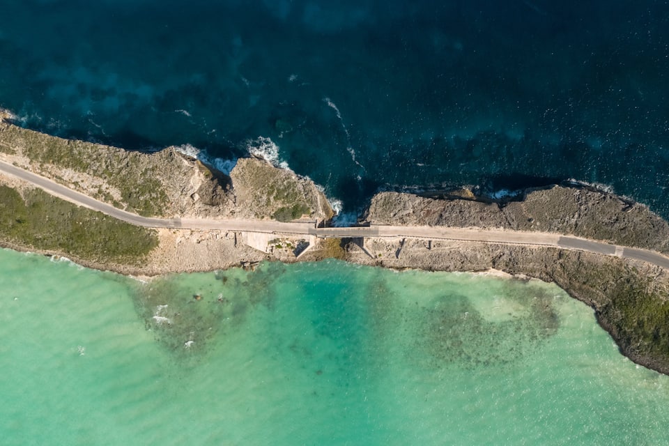 An aerial view of a coastal road with a bridge crossing a narrow waterway.