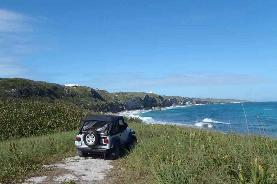 A jeep on a coastal path with ocean waves in the background.
