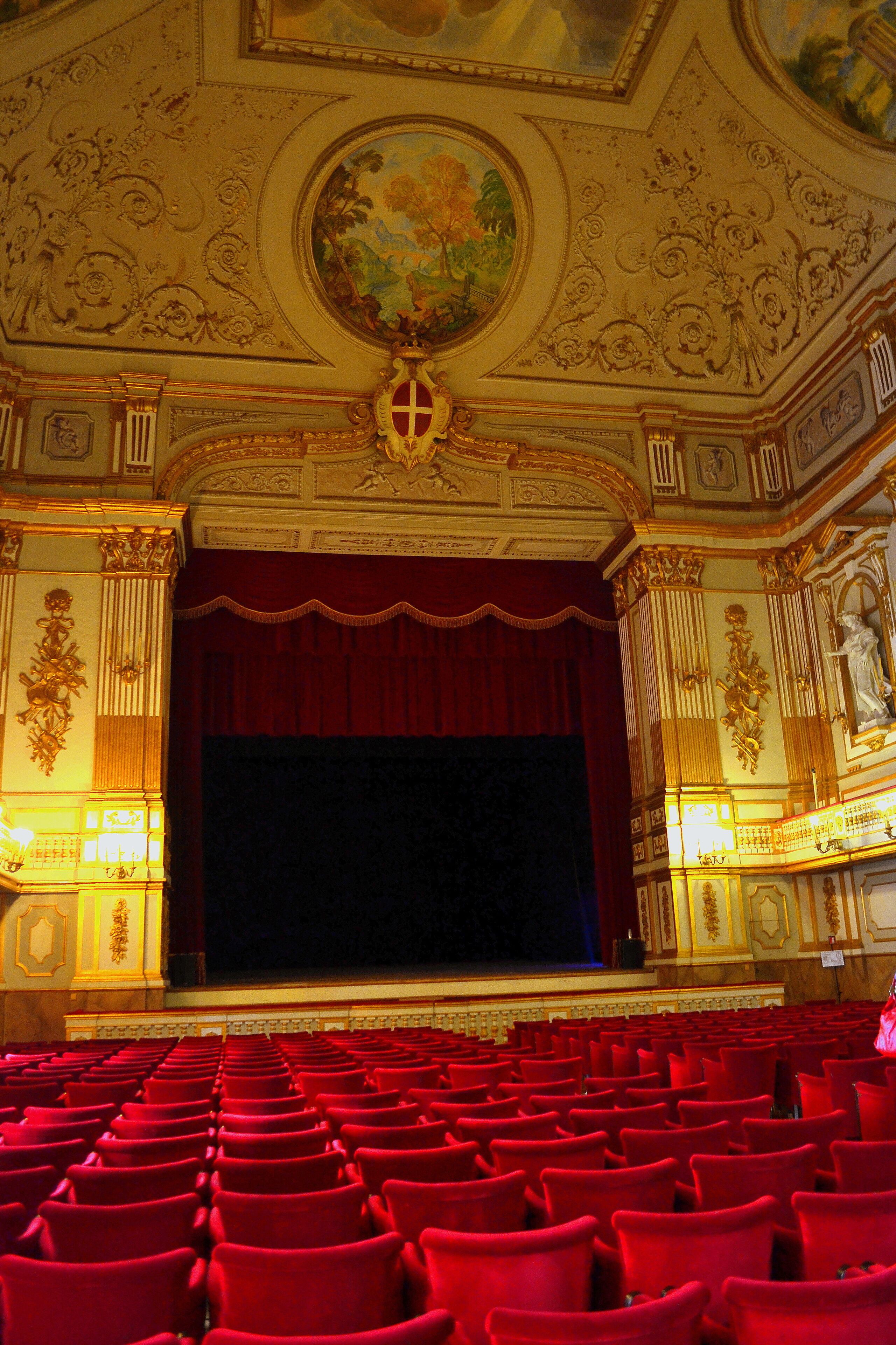 Hall of the historic Italian Theater San Carlo in Naples. The photo shows a stage with a red curtain and red chairs for the audience