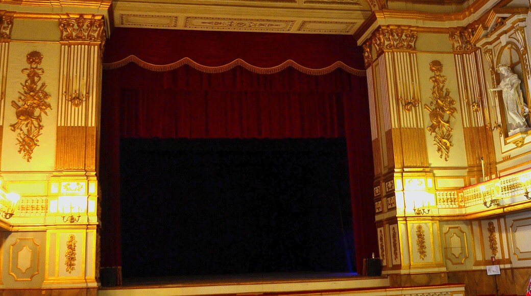 Hall of the historic Italian Theater San Carlo in Naples. The photo shows a stage with a red curtain and red chairs for the audience
