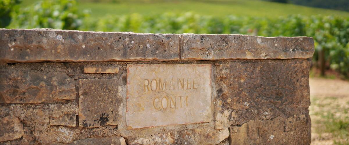 A stone wall with the inscription "ROMANEE CONTI" and a vineyard in the background.