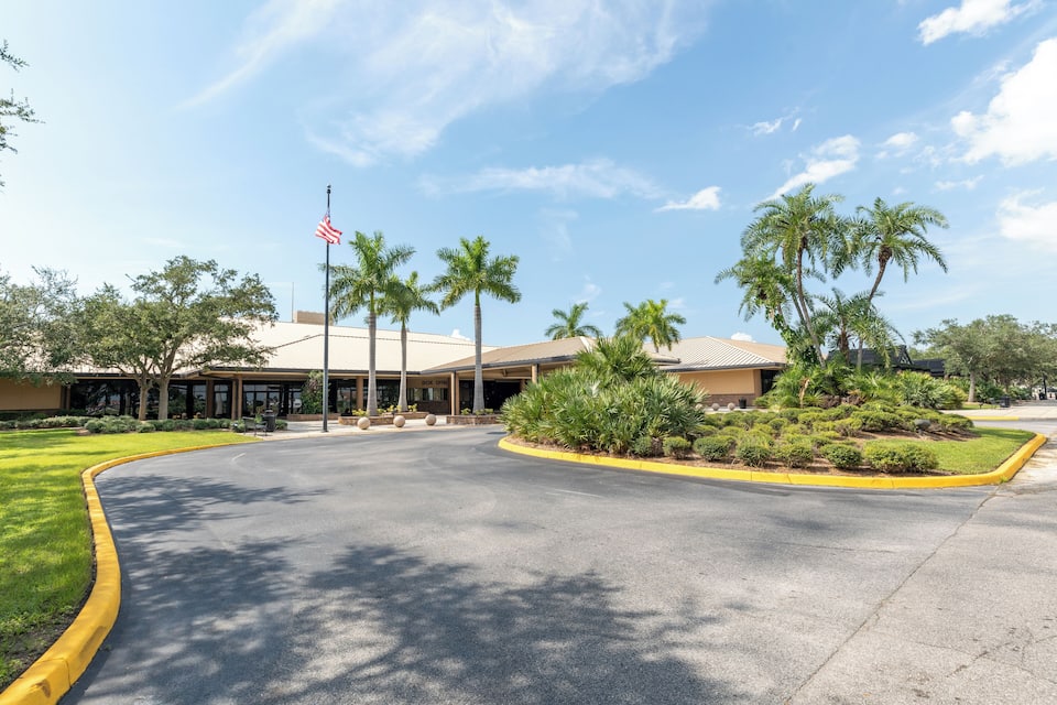 A building with an American flag, palm trees, and a curved road.