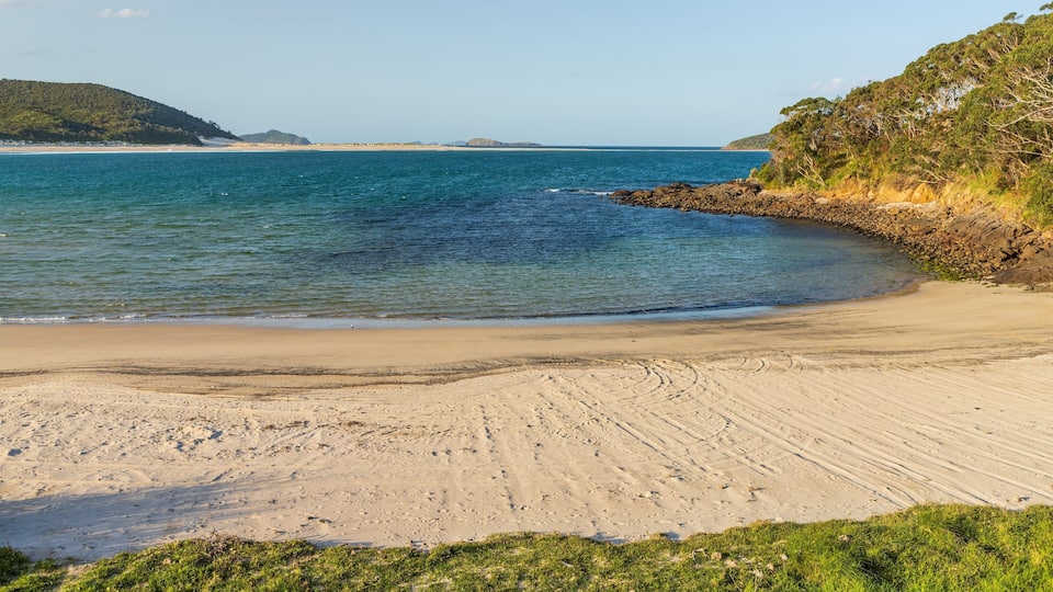 A sandy beach with gentle waves, a rocky shoreline, and distant hills.